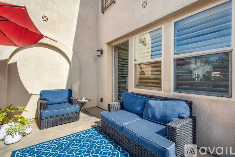 A patio with a blue couch, a matching ottoman, and a red umbrella.