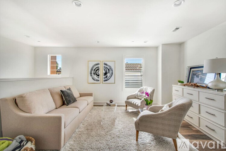 A living room with a beige couch, a chair, and a table with a vase of flowers on it.