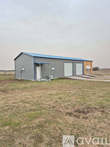 A small metal building with a blue roof is situated in a grassy field.