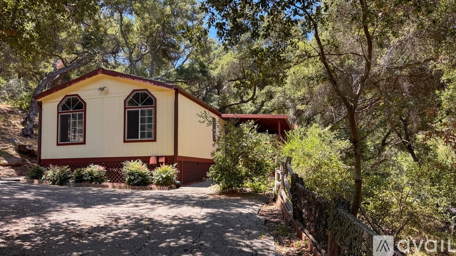 A small house is surrounded by trees and a dirt path leads to it.