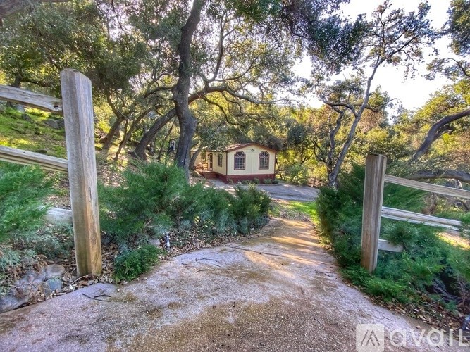A small house is surrounded by trees and a dirt path leads to it.