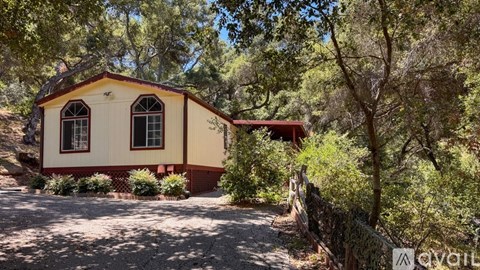 A small house is surrounded by trees and a dirt path leads to it.