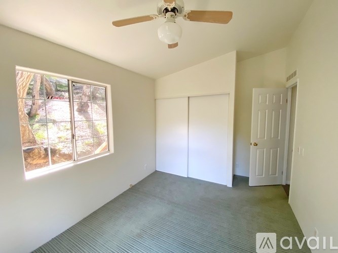 A room with a ceiling fan and a window overlooking a backyard.