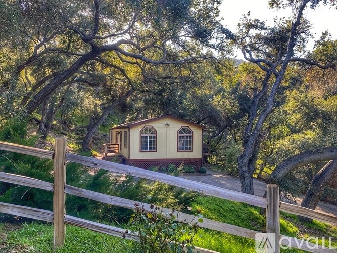 A small house is surrounded by trees and a wooden fence.