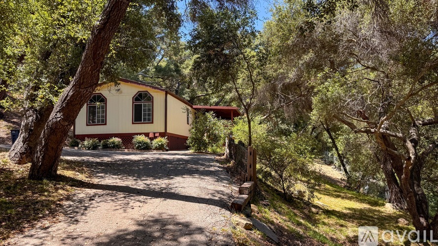 A small house with a red roof is surrounded by trees and greenery.