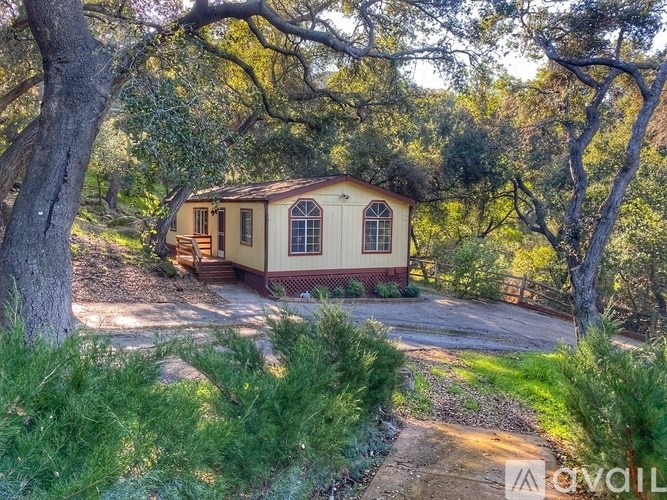 A small house with a red roof is surrounded by trees and greenery.