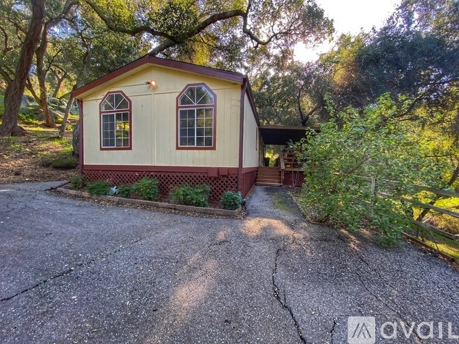 A small house with a red brick border is surrounded by greenery.