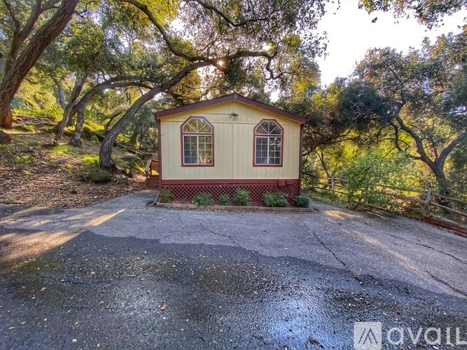 A small house with a red fence is surrounded by trees.