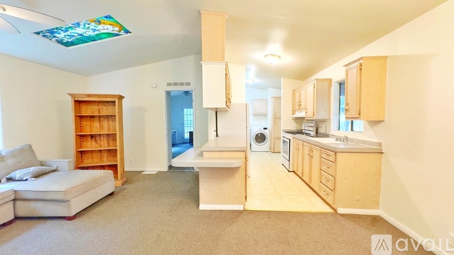 A living room with a couch, a bookshelf, and a kitchen area with a sink and stove.