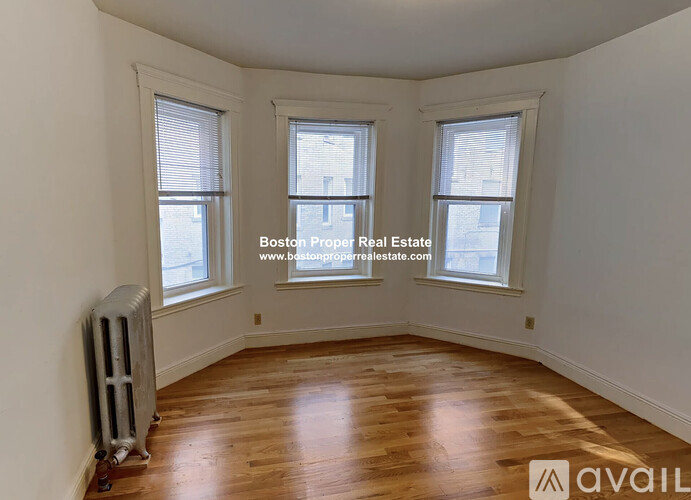 A room with wooden floors and two windows is available for rent.