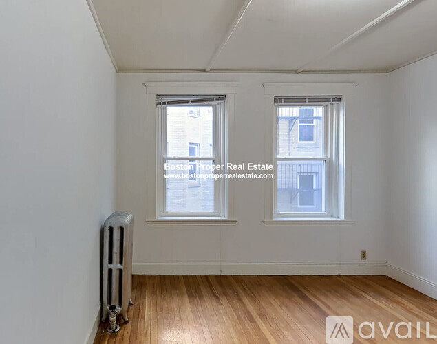 A room with wooden floors and two windows, one of which has a view of a building outside.