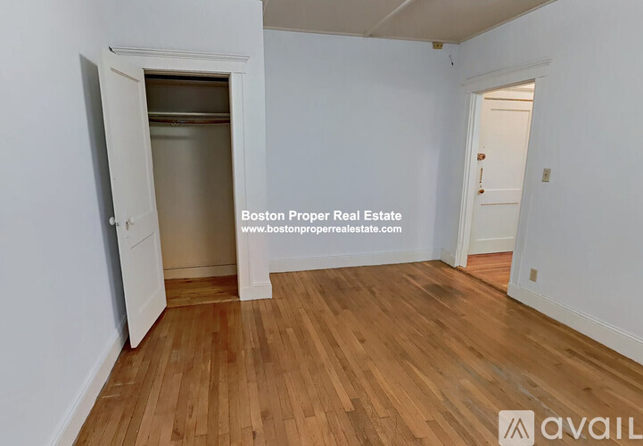 A room with wooden flooring and white walls, with a doorway leading to another room.