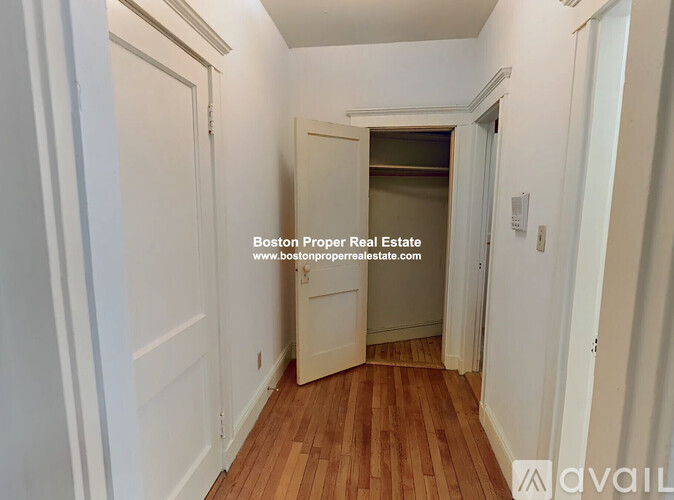 A hallway with wooden floors and white walls leading to a door.