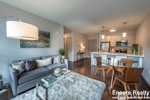 A well-lit living room with a grey sofa and a glass coffee table.