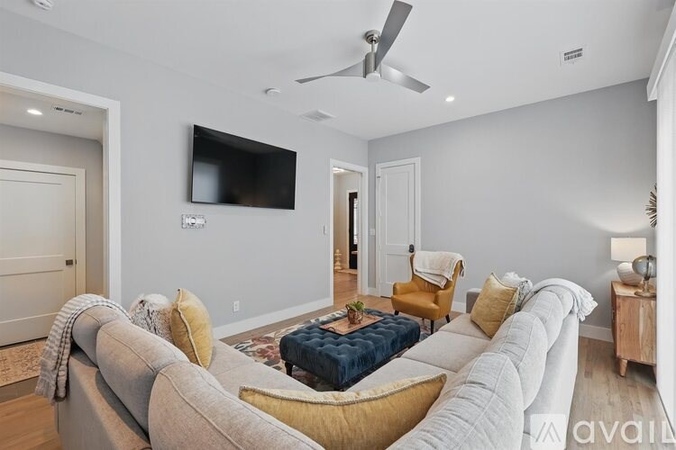 A living room with a grey couch, a blue ottoman, a yellow chair, and a flat screen TV mounted on the wall.