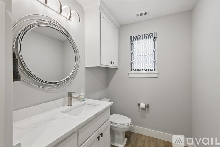 A bathroom with a toilet, sink, mirror, and cabinetry.