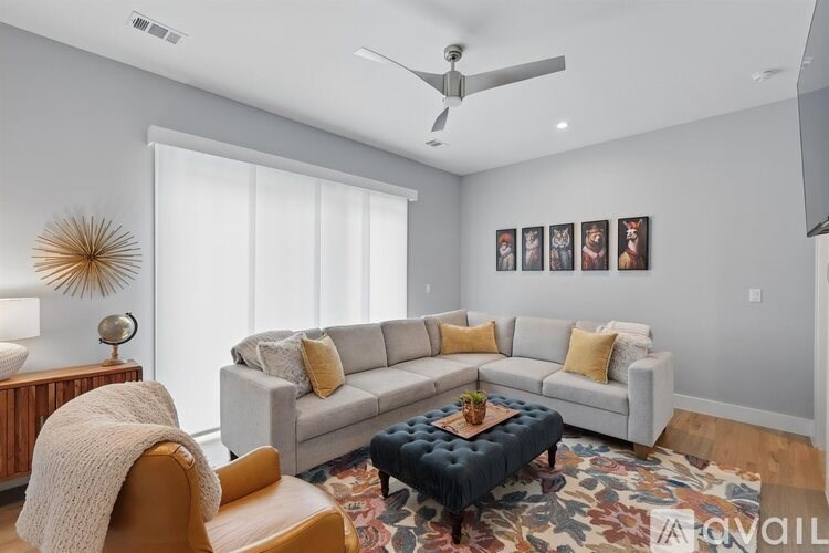 A living room with a grey couch, a yellow chair, a wooden side table, a ceiling fan, and a rug.