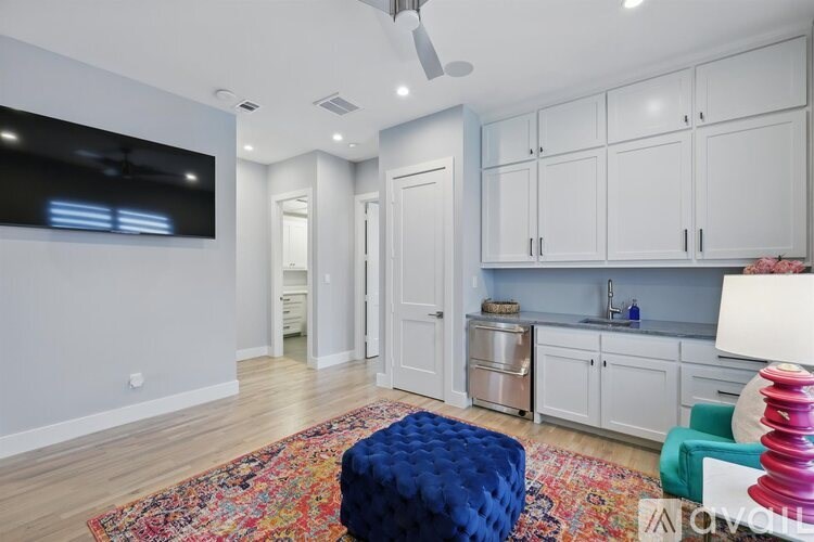 A living room with a blue ottoman and a television on the wall.