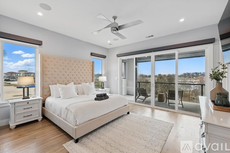 A bedroom with a large bed, a ceiling fan, and a view of the outside through the windows.