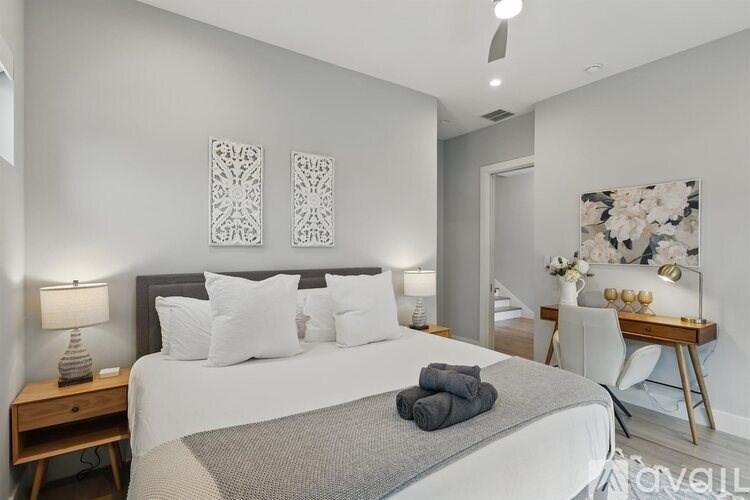 A bedroom with a large bed, a desk with a chair, and a painting on the wall.