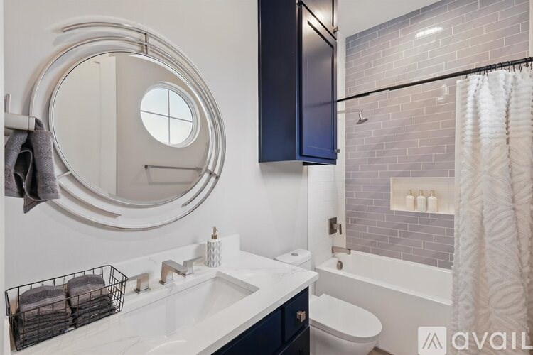 A bathroom with a round mirror, sink, and bathtub.