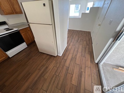 A kitchen with a white fridge and wooden floors.