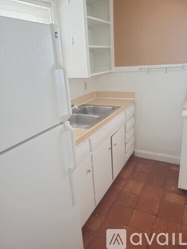A kitchen with a white refrigerator and brown tiled floor.
