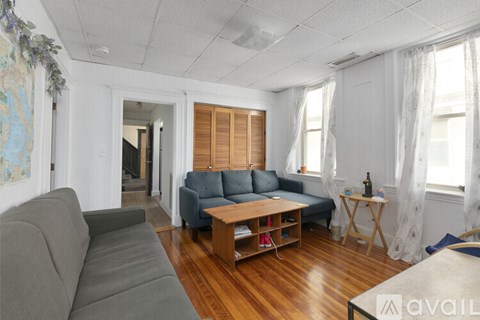 A living room with a grey couch, a grey sofa, a wooden table and a white wall.