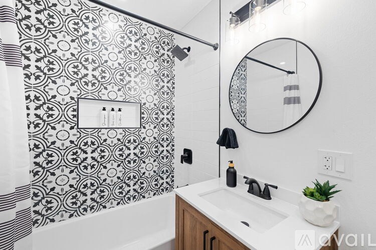 A bathroom with a black and white tiled shower and a round mirror above a sink.