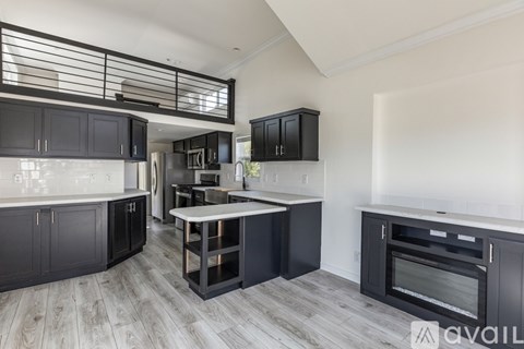 A modern kitchen with black cabinets and a wooden floor.