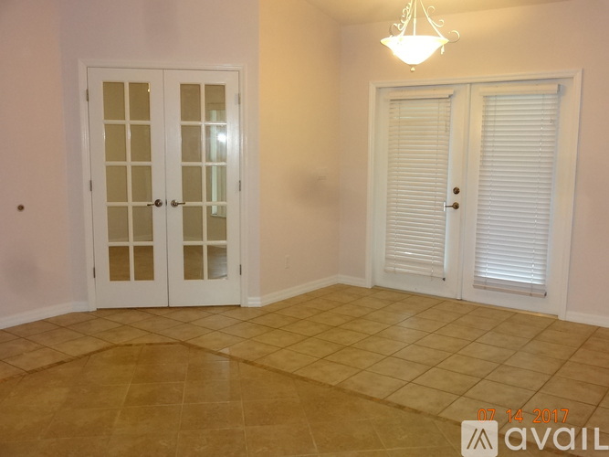 A room with a tan floor and white walls has two doors and a chandelier.