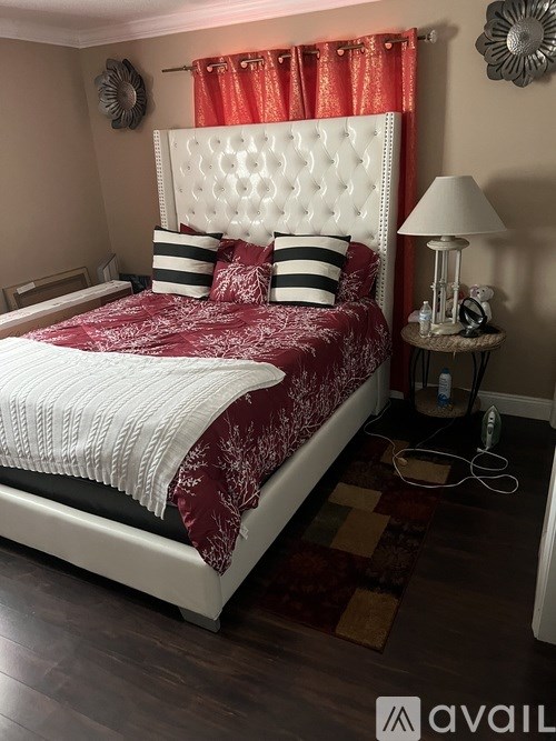 A bed with a white headboard and red bedspread with a white pillow and a small table with a lamp on it.