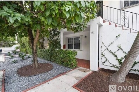 A tree in a brown circle is in front of a white building with a black railing.