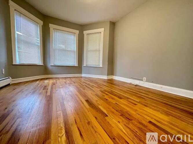 A room with wooden flooring and two windows.