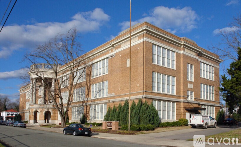 A large red brick building with a white trim around the windows and a white van parked in front.