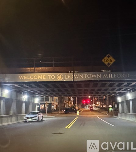 A car is driving under a bridge that says "Welcome to Downtown Milford".