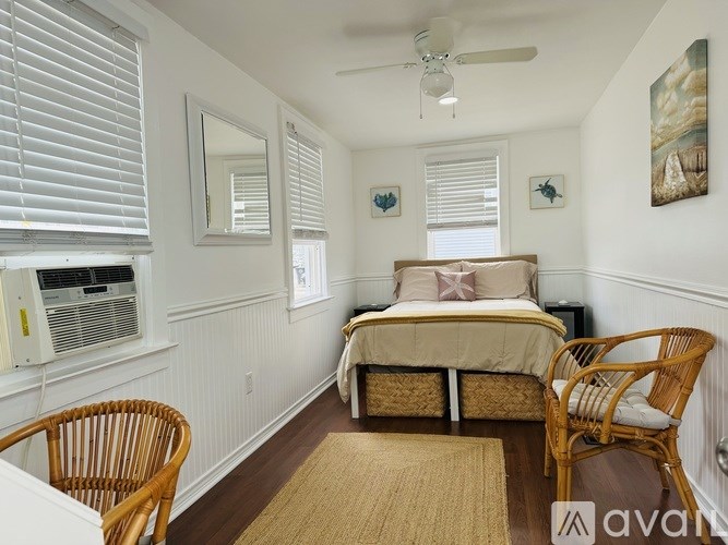 A bedroom with a bed, two chairs, and a ceiling fan.