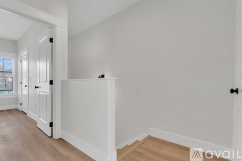 A room with white walls and wooden flooring, with a door on the left and a window on the right.