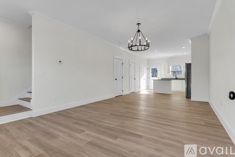 A spacious room with wooden flooring and a chandelier hanging from the ceiling.