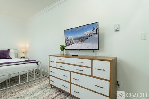A bedroom with a bed, a dresser with a television on top, and a rug on the floor.