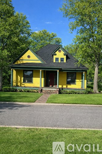 A yellow house with a black roof and a tree in front.