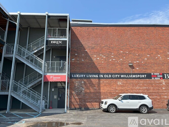 A white car is parked in front of a building with a sign that says "LUXURY LIVING IN OLD CITY WILLIAMSPORT.".