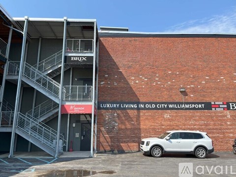A white car is parked in front of a building with a sign that says "LUXURY LIVING IN OLD CITY WILLIAMSPORT.".