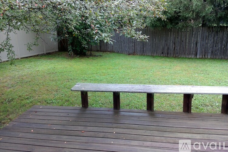 A wooden bench sits on a wooden deck in a backyard.