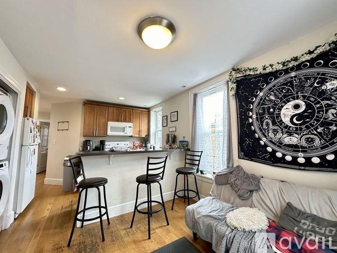 A living room with a couch, chairs, and a large tapestry on the wall.