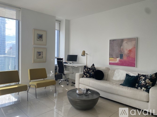 A living room with a yellow chair, a white couch, and a painting on the wall.