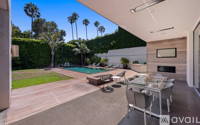 A modern outdoor patio area with a table and chairs overlooking a pool and lush greenery.