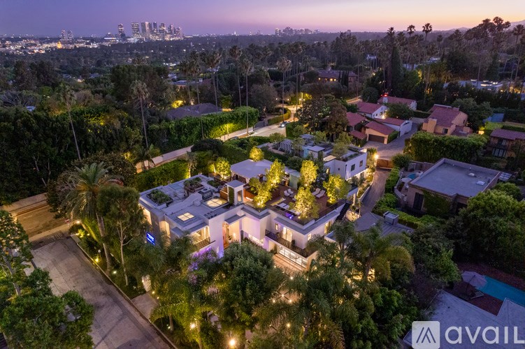 A large house with a swimming pool is surrounded by trees and is lit up at night.