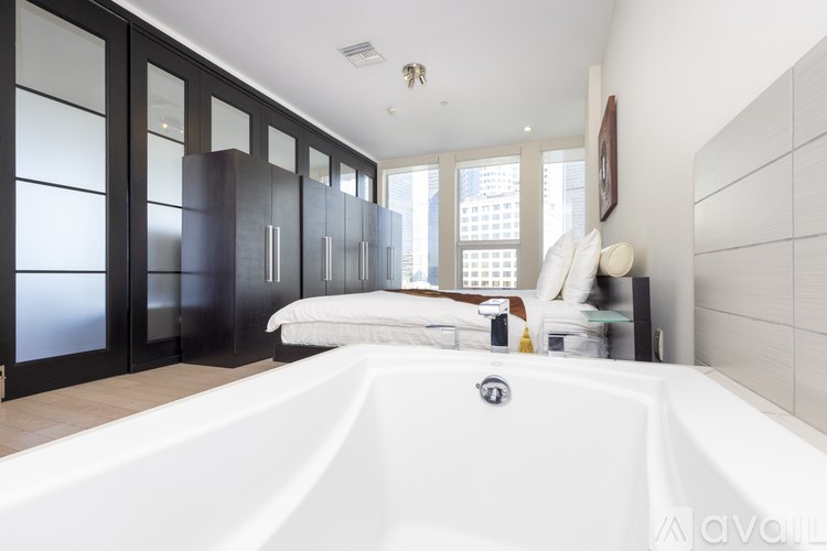 A white bathtub is in a bathroom with a bed and a window.