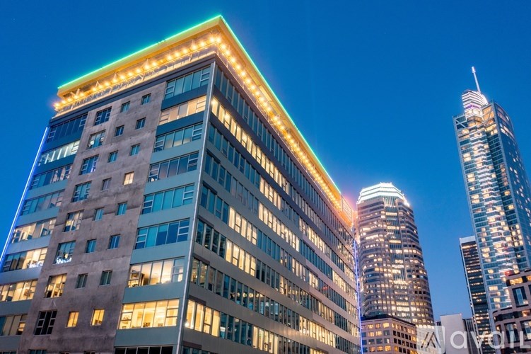 A tall building with a lit up facade stands next to a shorter building with a lit up facade.